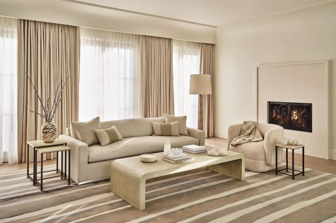 Modern neutral living room interior with a long cream sofa, matching armchair, coffee table, and a fireplace by The Ingalls.