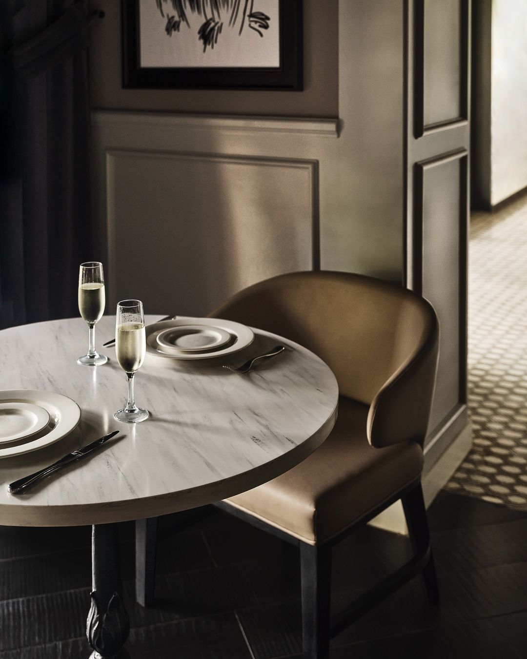 Elegant dining table setting with two champagne flutes, plates, and silverware in a warmly lit, upscale indoor environment.