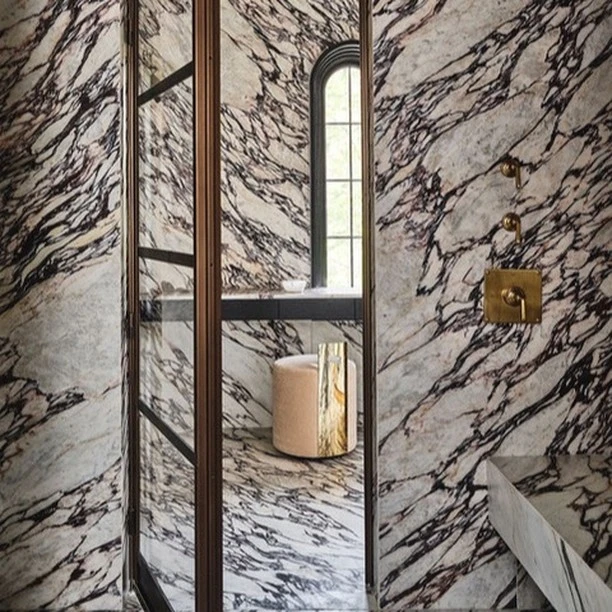 Luxurious bathroom interior featuring marble walls, a glass shower enclosure, a plush stool, and elegant brass fixtures, exuding sophisticated design.