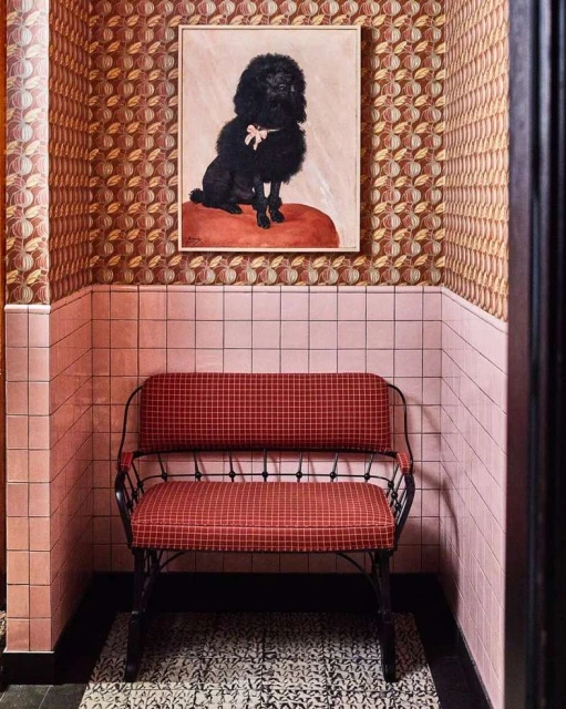 Interior of a waiting room with a red bench, a framed portrait of a poodle, pink tile walls, and patterned brown wallpaper.