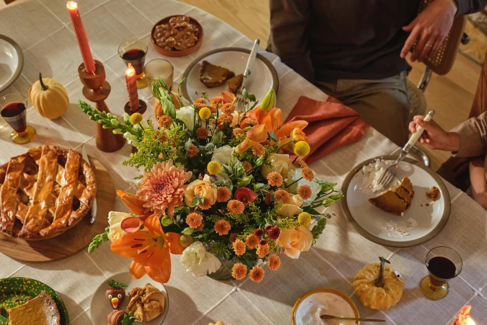 Overhead shot of a holiday dinner table setting with floral centerpiece, pumpkin pie, decorative pumpkins, and lit candles.