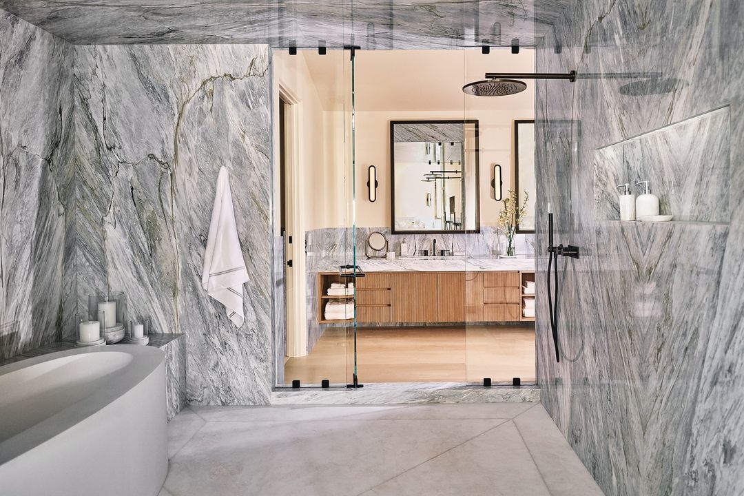 Modern bathroom interior with marble walls, bathtub, walk-in shower, and double sink vanity with mirrors and sconces, creating a spa-like atmosphere.