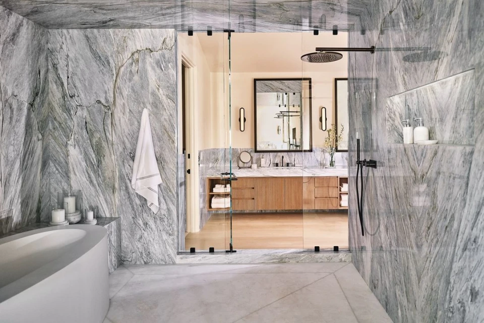 Modern bathroom interior with marble walls, bathtub, walk-in shower, and double sink vanity with mirrors and sconces, creating a spa-like atmosphere.