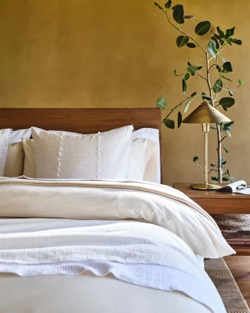 Bedroom interior with a wooden headboard, neutral bedding, and a bedside table lamp, creating a serene and inviting atmosphere.
