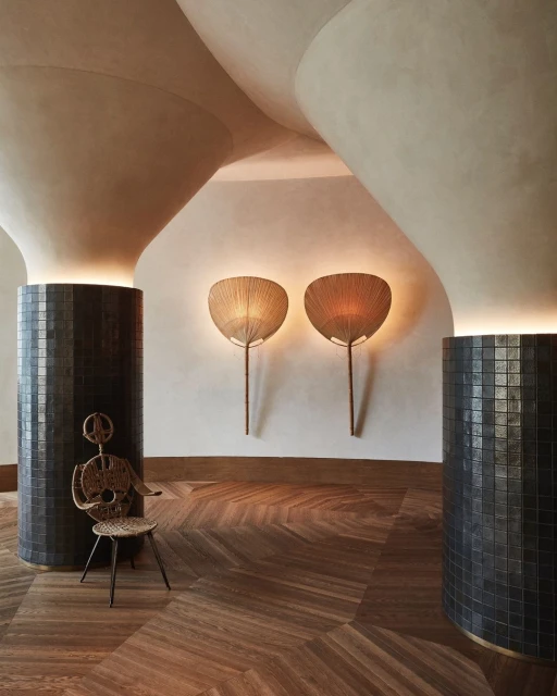 Interior design showcases two wicker fan-shaped lamps on the wall, a unique chair, and geometric columns in a herringbone floor room.