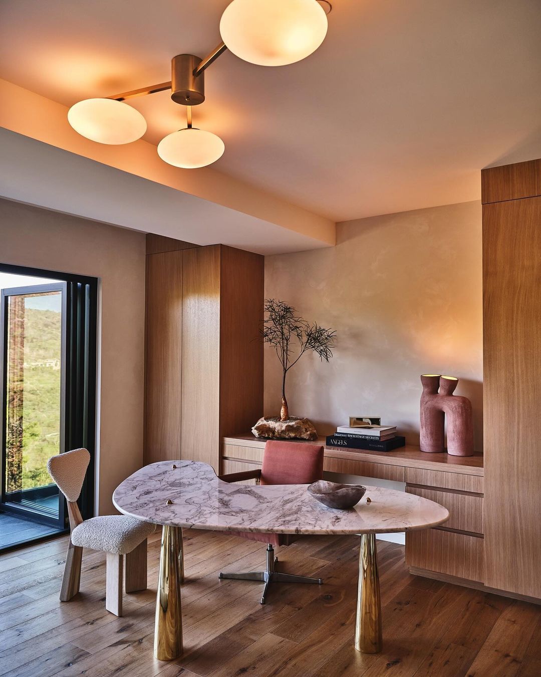 Modern interior design featuring a marble desk with gold legs, a stylish chair, wood cabinets, and a unique ceiling light fixture.