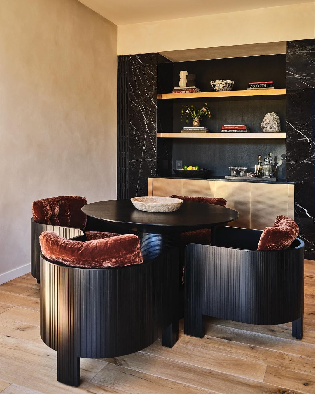 Interior design featuring a round dark wood table surrounded by four unique black chairs with plush rust-colored cushions on a light wood floor.