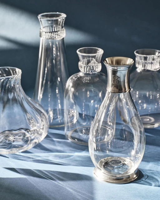 Elegant display of clear glass decanters and vases with silver accents on a blue surface, creating a sophisticated table setting.