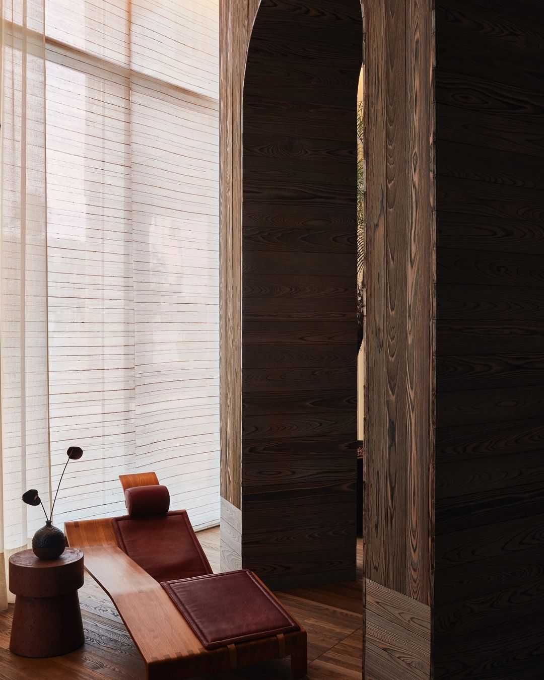 Interior space featuring a wooden lounge chair with leather cushions next to a small side table with a decorative vase.
