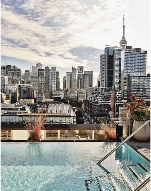 Rooftop infinity pool with city skyline view featuring skyscrapers and the CN Tower on a bright day with wispy clouds.