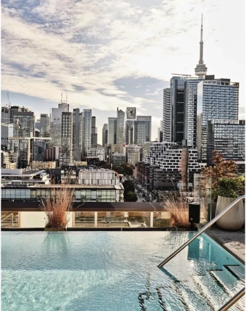Rooftop infinity pool with city skyline view featuring skyscrapers and the CN Tower on a bright day with wispy clouds.