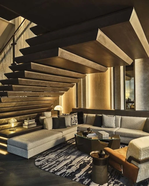 Interior view of a modern living room featuring a sectional sofa, tiered staircase, and patterned rug in neutral tones.