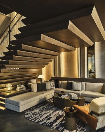 Interior view of a modern living room featuring a sectional sofa, tiered staircase, and patterned rug in neutral tones.