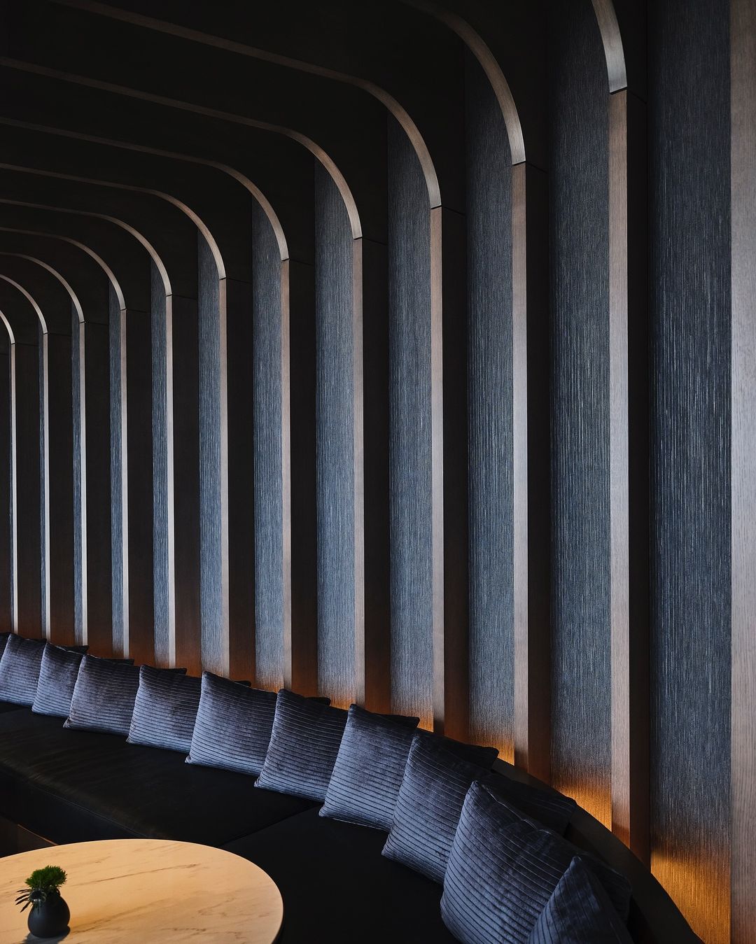 Interior design featuring a curved, dark wooden wall with integrated lighting, creating a modern and sophisticated architectural space.