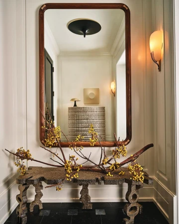 Interior hallway with a wooden framed mirror above a console table decorated with yellow berries in front of a white wall.