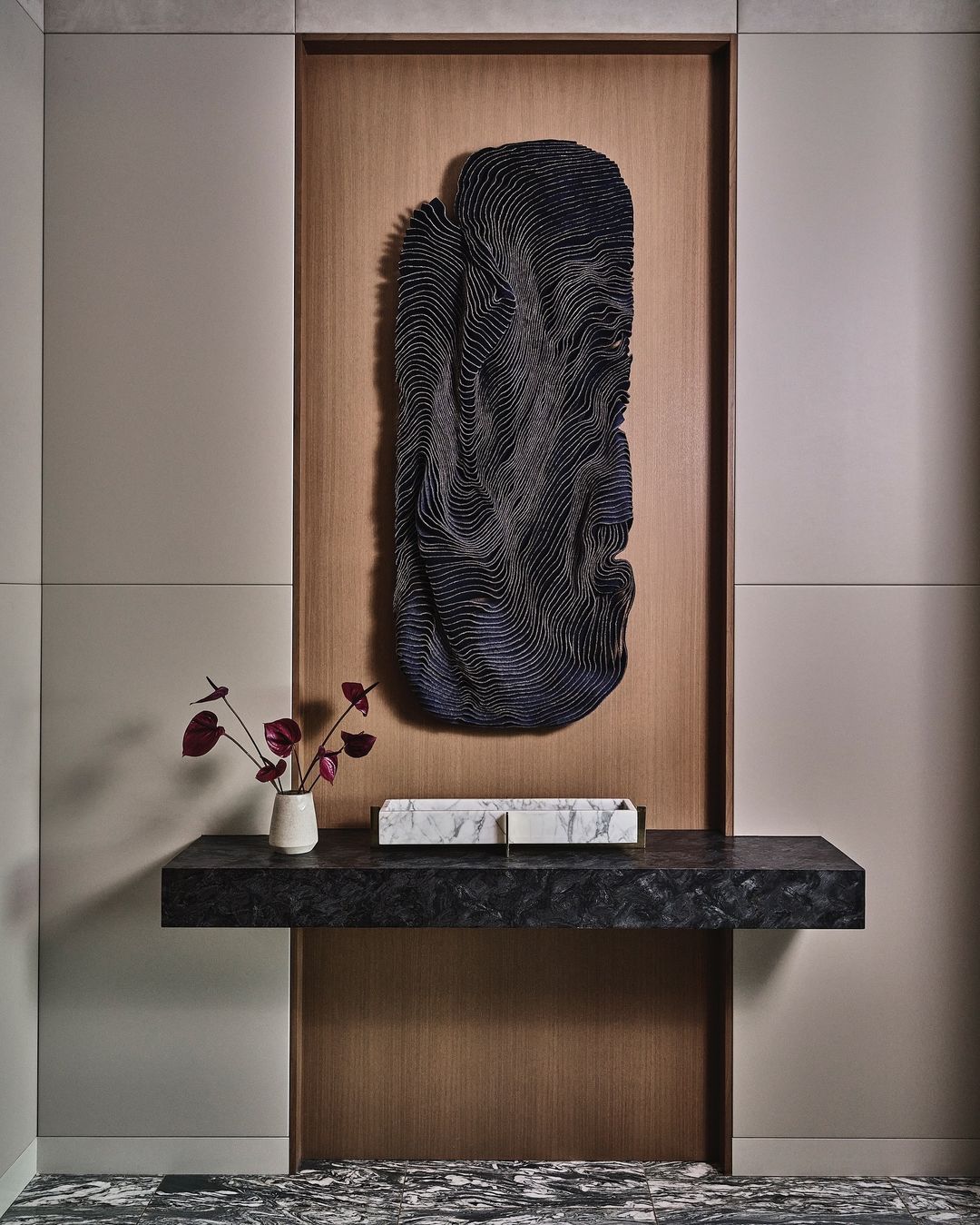 Contemporary interior showcasing a black console table with marble accents, adorned with a vase of dark red flowers and a black abstract sculpture.