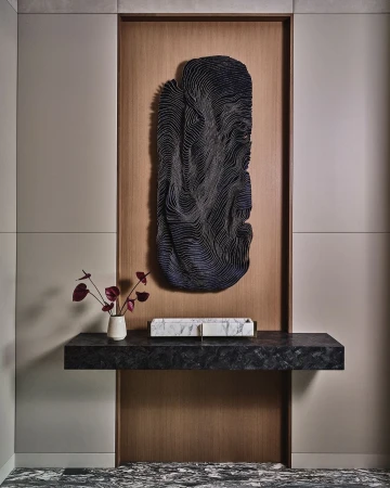 Contemporary interior showcasing a black console table with marble accents, adorned with a vase of dark red flowers and a black abstract sculpture.