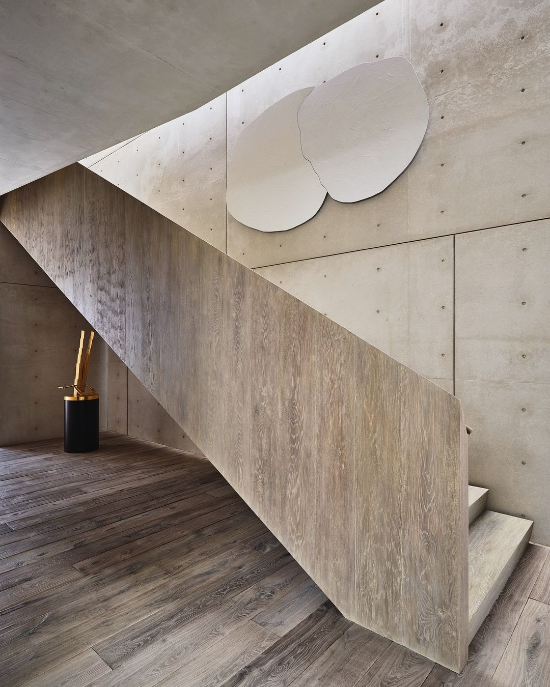 Interior staircase featuring light wood stairs, concrete walls, and unique white round wall art in a modern architectural design.