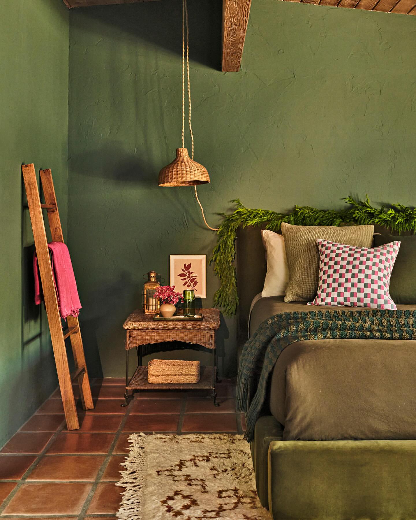Bedroom interior featuring an olive green color scheme, complete with bed, nightstand, woven lamp, blanket, pillows, and a rustic wooden ladder.