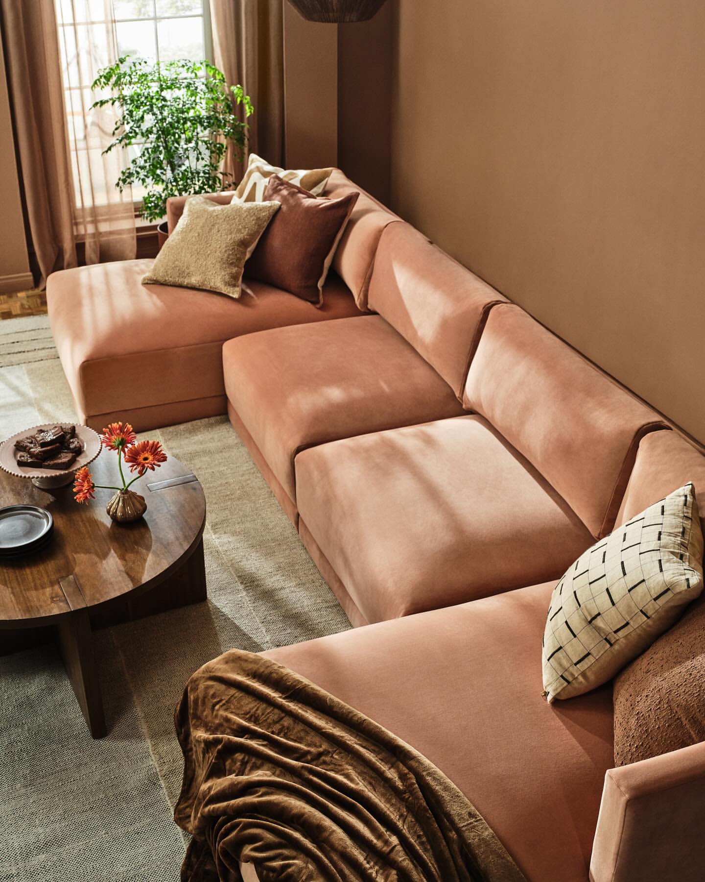 Interior design featuring a sectional sofa in a living room setting with a round coffee table, throw blanket, and natural light from a window.