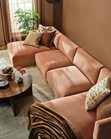 Interior design featuring a sectional sofa in a living room setting with a round coffee table, throw blanket, and natural light from a window.