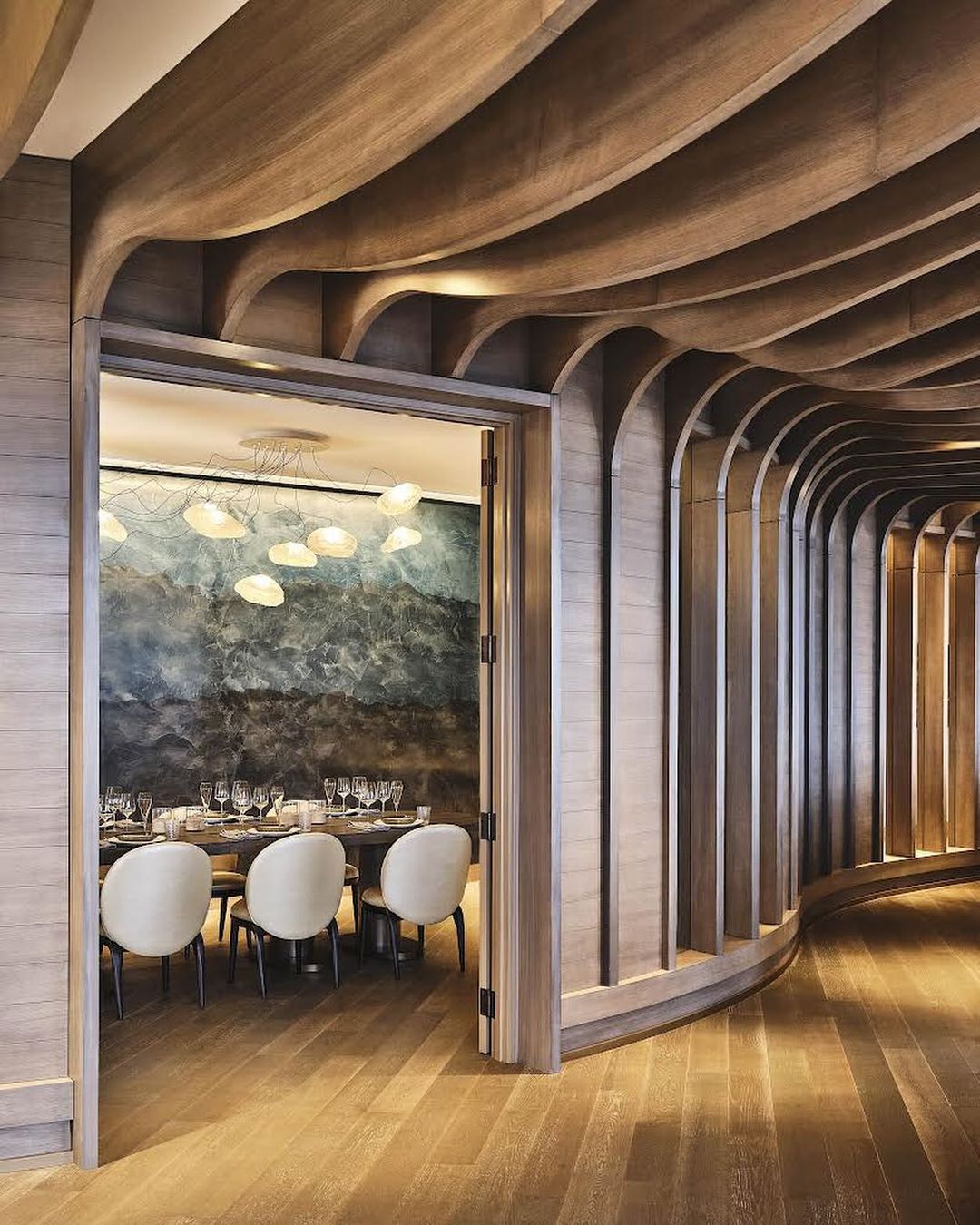 Interior design of a restaurant dining room featuring a wood ceiling, light fixture, a long table, chairs and a large wall mirror.