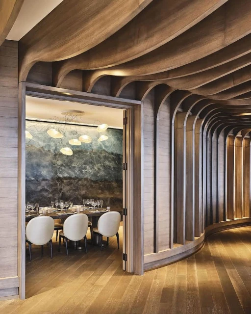 Interior design of a restaurant dining room featuring a wood ceiling, light fixture, a long table, chairs and a large wall mirror.