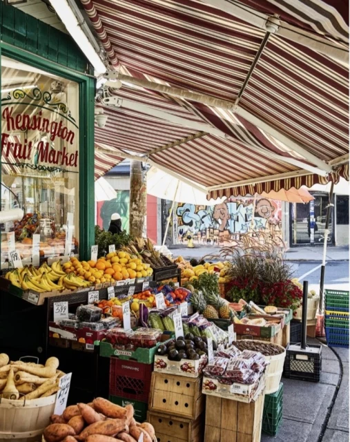Fruit stand bursting with color: bananas, oranges, strawberries, pineapples, avocados, sweet potatoes, and parsnips on display outside.