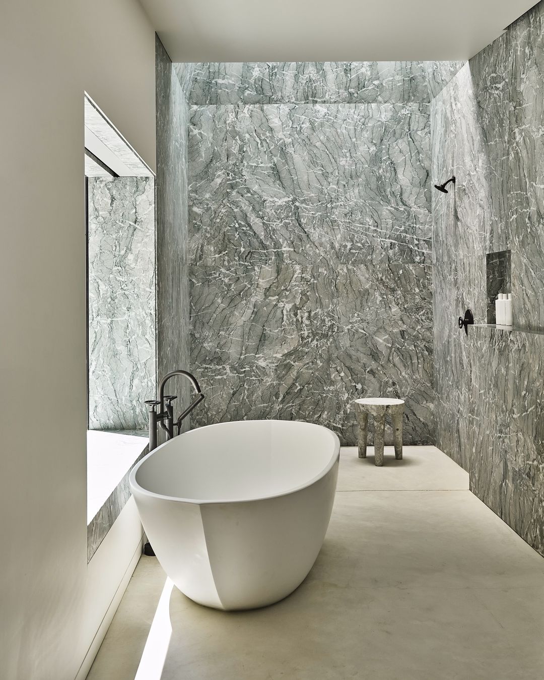 Modern bathroom interior with a white, egg-shaped freestanding bathtub, grey marble walls, and a window providing natural light.