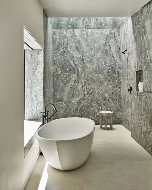 Modern bathroom interior with a white, egg-shaped freestanding bathtub, grey marble walls, and a window providing natural light.