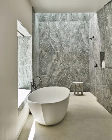 Modern bathroom interior with a white, egg-shaped freestanding bathtub, grey marble walls, and a window providing natural light.