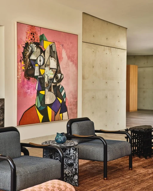 Living room interior featuring an abstract painting in pink hues, two gray armchairs, and a unique side table with a dark blue vase.