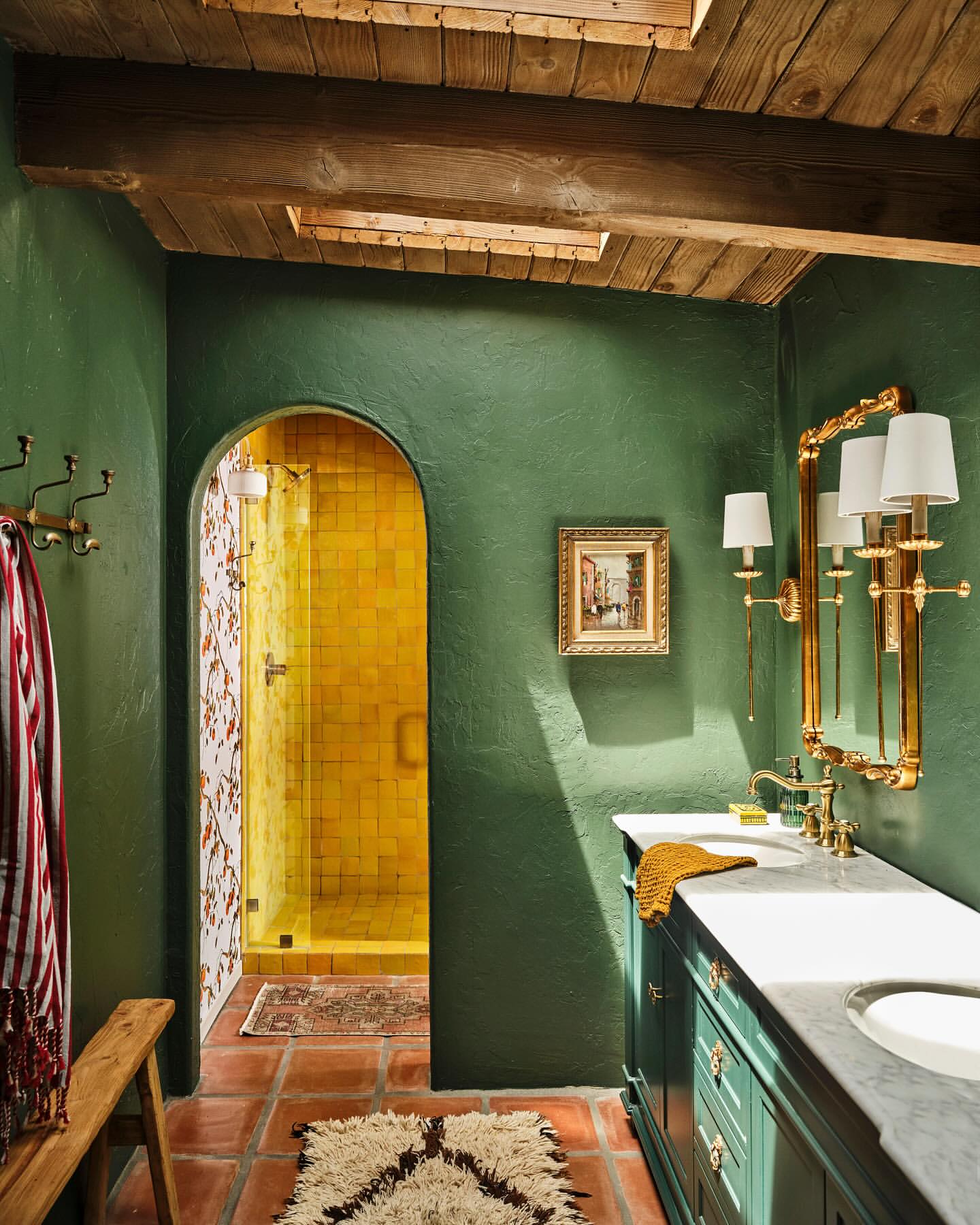 Bathroom interior with green walls, terracotta tile floors, rustic wood ceiling, marble-top vanity, and walk-in shower with yellow tile.