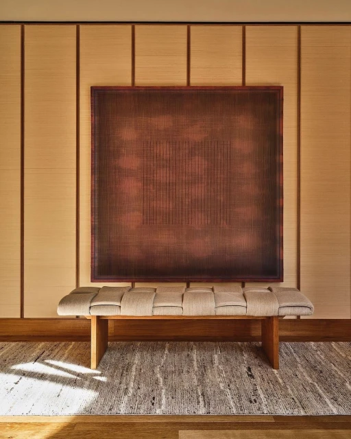 Abstract artwork featuring a copper color palette, displayed above a modern upholstered bench with wood accents, neutral color scheme, indoors.