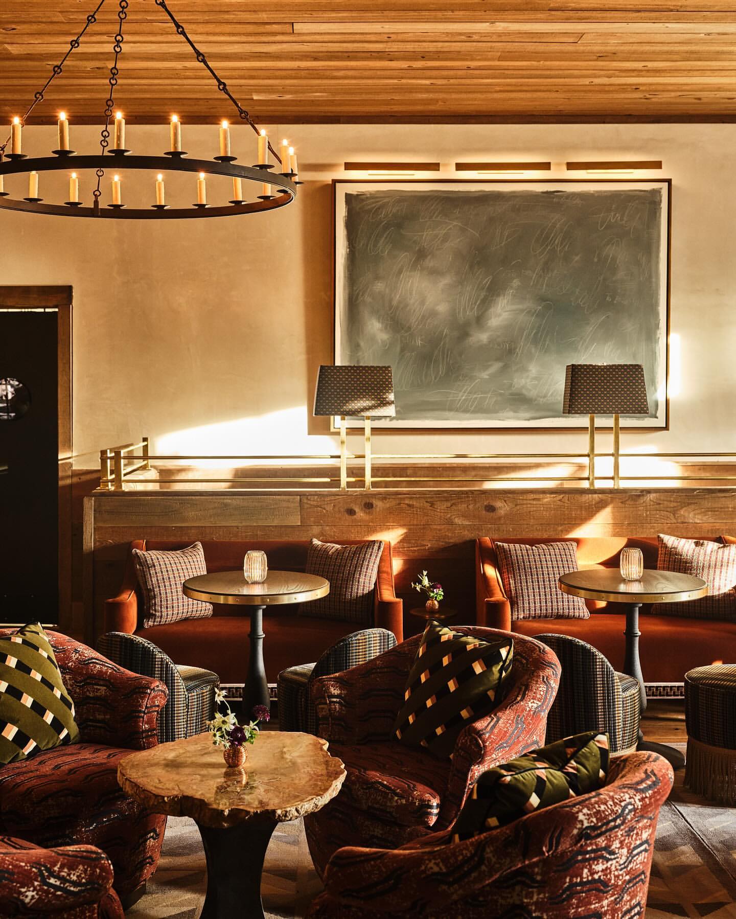 Interior of a stylish lounge with comfortable seating, including patterned armchairs and sofas, lit by a chandelier and lamps.