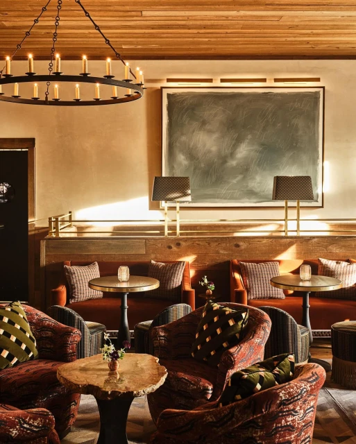 Interior of a stylish lounge with comfortable seating, including patterned armchairs and sofas, lit by a chandelier and lamps.