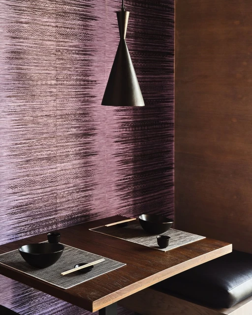 Dining nook with dark wood table, black bowls and placemats, illuminated by a single pendant light against a textured wall.