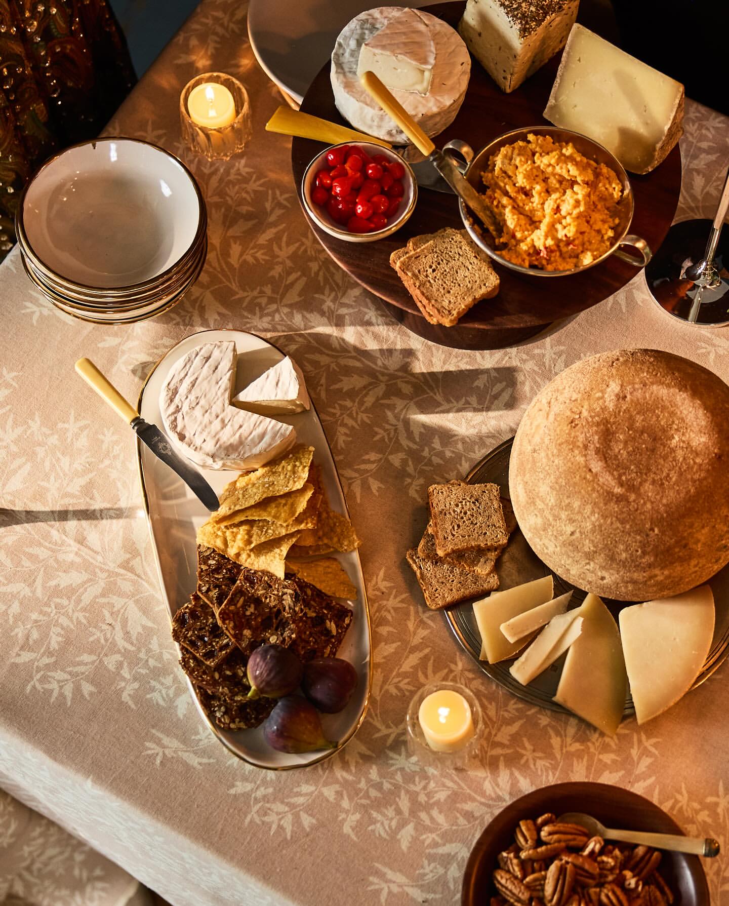 Overhead shot of an elegantly arranged cheese board with various cheeses, crackers, figs, bread, nuts, and cherry preserves on a table.