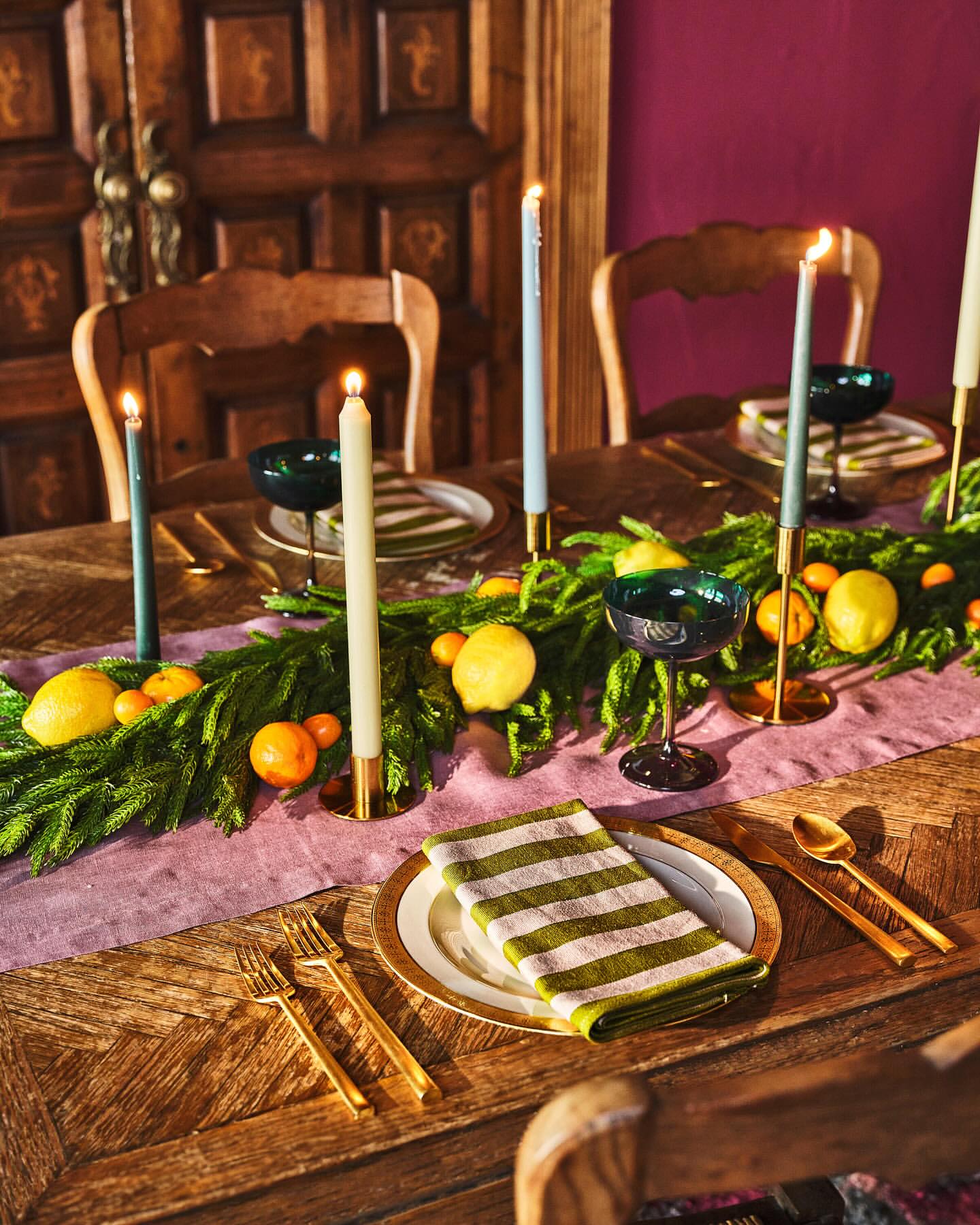 Elegant table setting with burning candles, gold flatware, garnished with lemons and greenery, evoking a warm, festive ambiance.