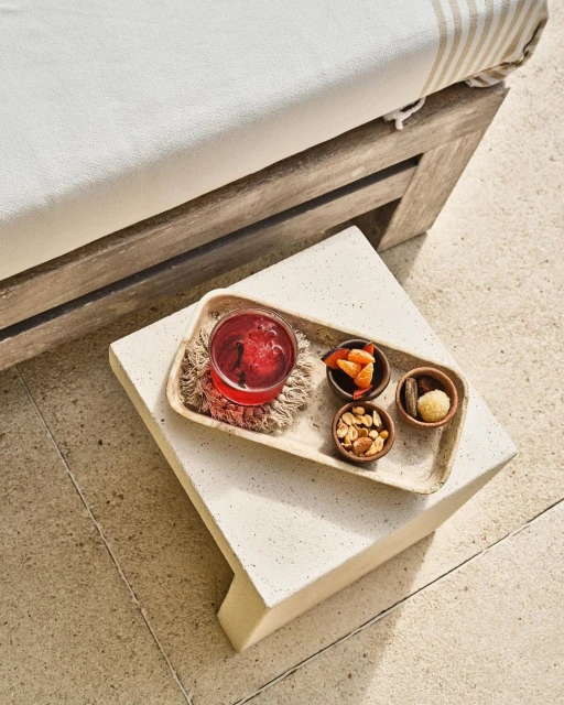 Overhead shot of a tray with a red drink and snacks on a stone table next to a chaise lounge.  Ideal for food and beverage.