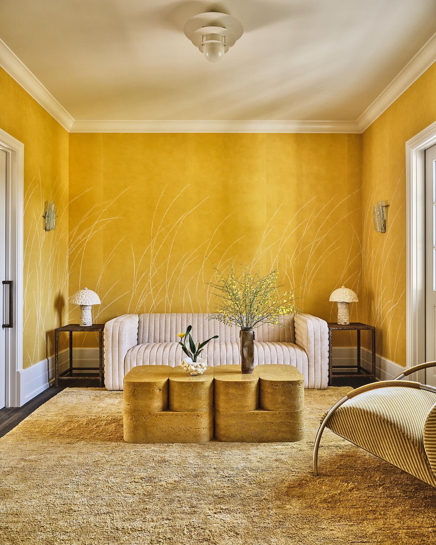 Interior view of a living room featuring a cream-colored sofa, geometric coffee table, area rug, and yellow walls with subtle decorations.