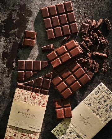 Overhead shot of broken chocolate bars with paper wrappers scattered on a dark surface, highlighting food photography and dark brown hues.