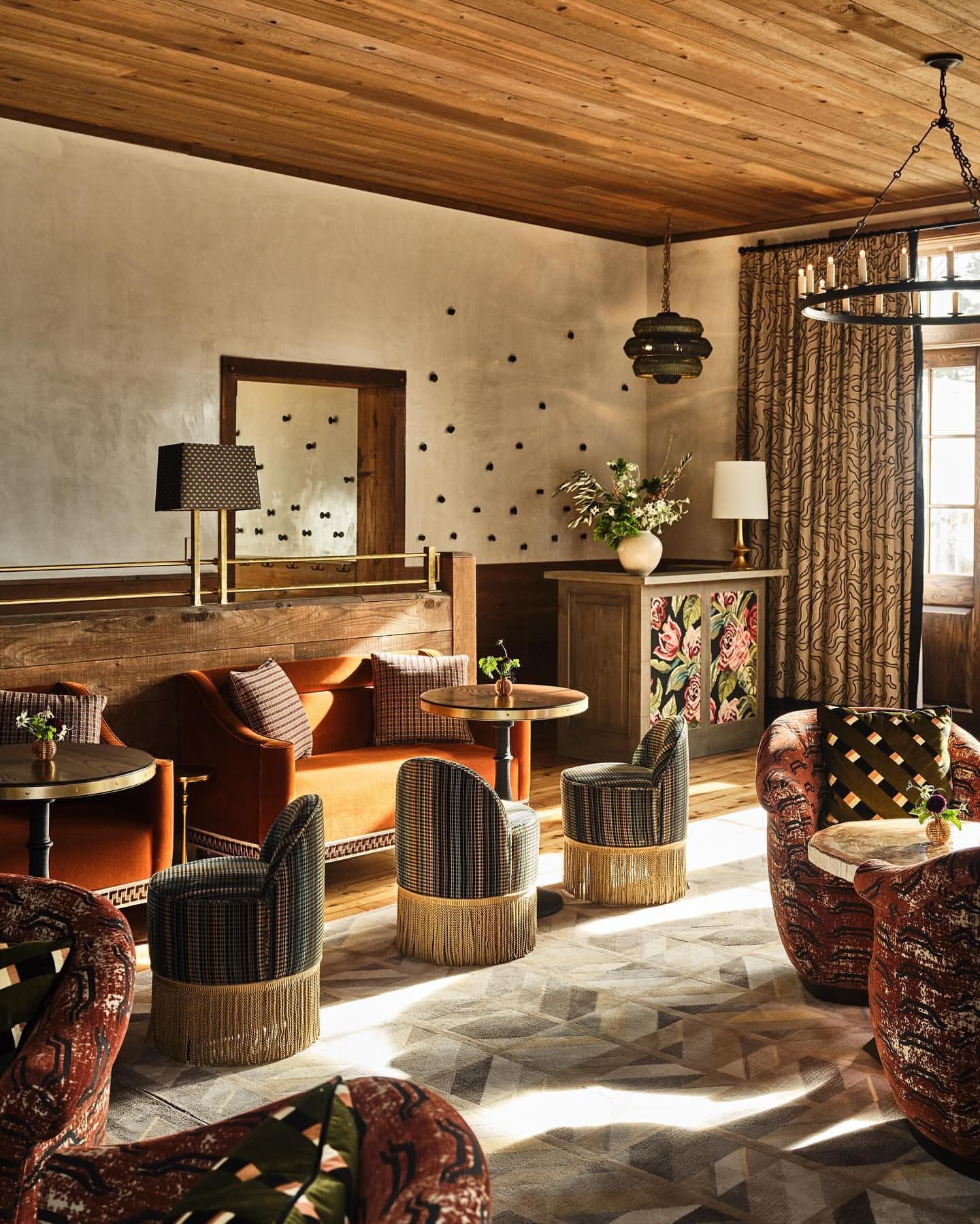 Interior lounge area with seating arrangements including patterned chairs, rust-colored sofas, and small tables under wood plank ceiling.