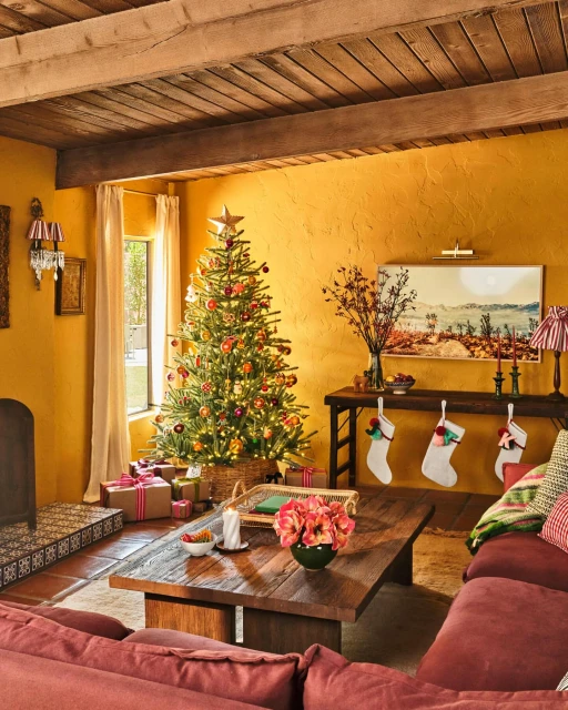 Festive living room with a decorated Christmas tree adorned with ornaments and lights, presents, stockings, and a cozy seating area.