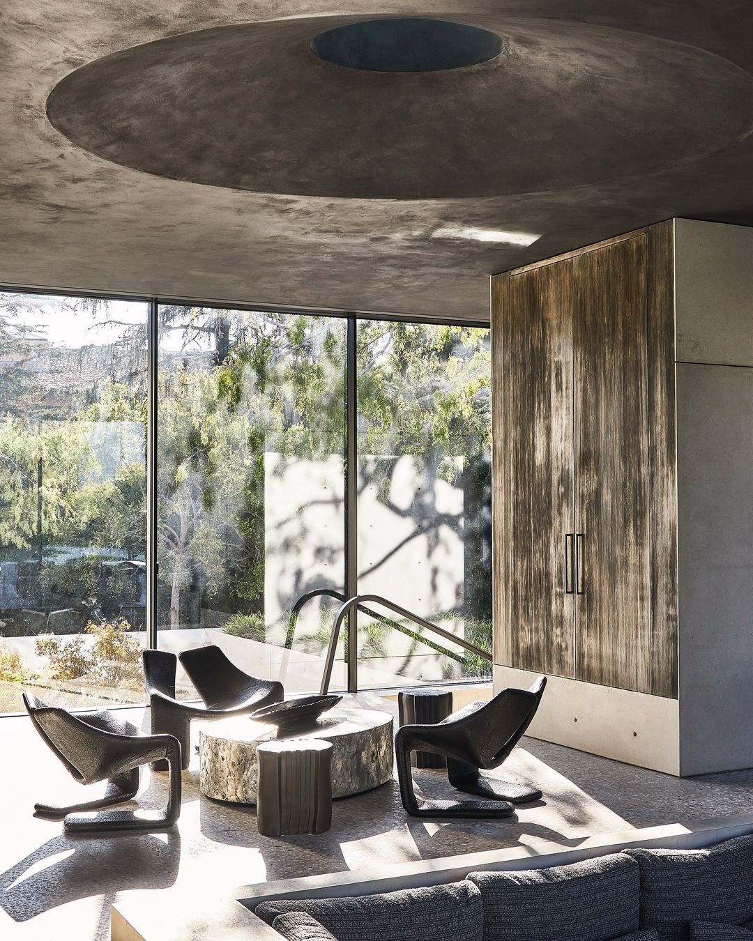 Interior space features four modern black chairs around a concrete table, natural light from large windows, and a unique ceiling design.