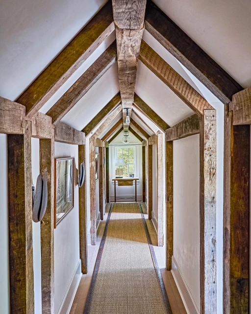 Hallway interior featuring reclaimed wood beams, white walls, and a woven rug. Interior design showcases rustic and modern elements.