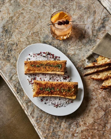 Overhead shot of two marrow bones on a plate with cocktail and bread, highlighting food and drink photography.