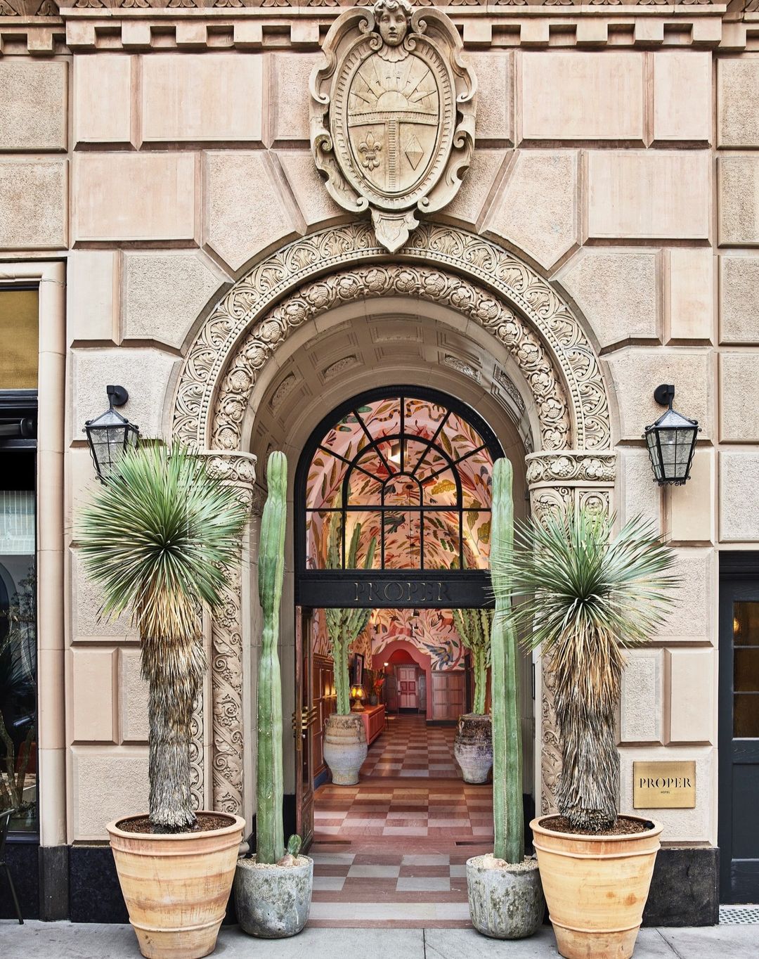 Exterior view of a hotel entrance with an arched doorway framed by potted cacti, showcasing architectural details and interior design.