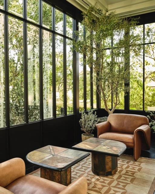Stylish interior with modern brown leather armchairs, geometric-patterned rug, dark window frames, potted tree, and tile-topped coffee tables.