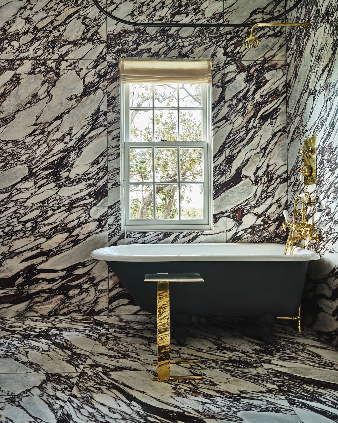 Bathroom featuring a freestanding tub, gold accents, and marble walls, creating an elegant and luxurious interior space.